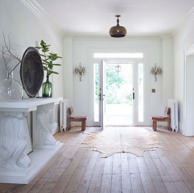 A-List 2024 - ELLE DECOR spare entry way with bleached wood flors and a white console with caryatid like pediments and a mirror over it and a shaggy green piece of artwork opposite