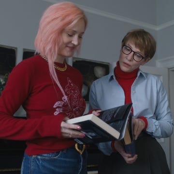 two individuals engaged in a discussion while holding books with another person observing in the background
