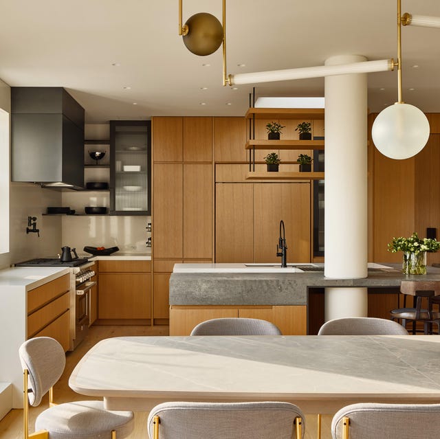 The A-List 2024 - ELLE DECOR a kitchen with a long rounded edge light wood dining table with matching chairs and honey colored cabinets in the back