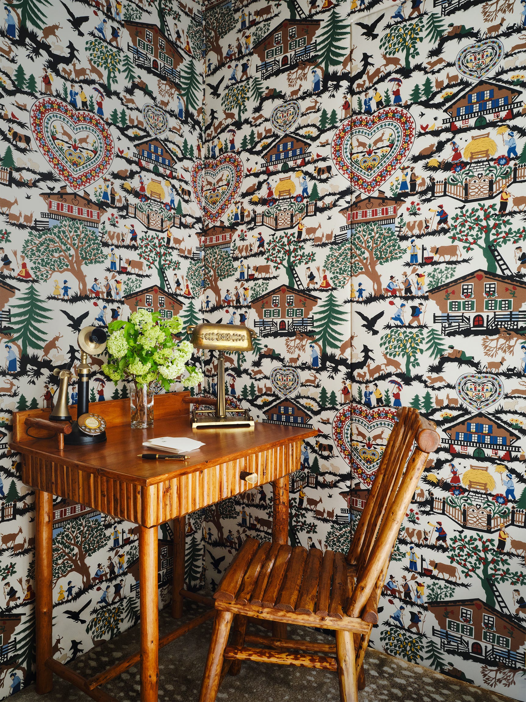 Rustic work space featuring a wooden table and chair against decorative wallpaper.