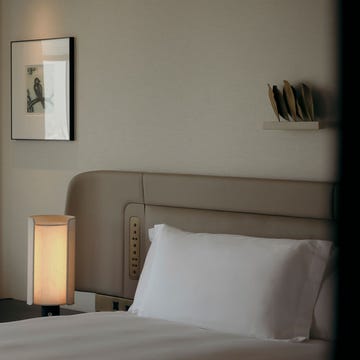 Interior view of a hotel room featuring a bed, chair, lamp, and artwork.