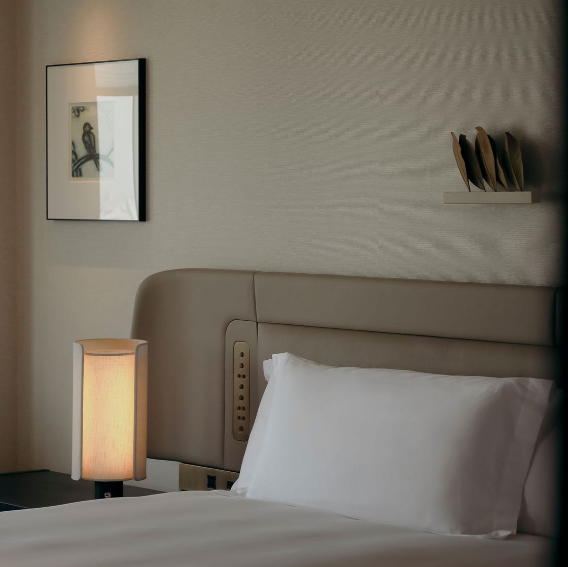 Interior view of a hotel room featuring a bed, chair, lamp, and artwork.