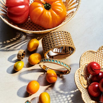 A composition of vibrant fruits and jewelry arranged on a textured surface.