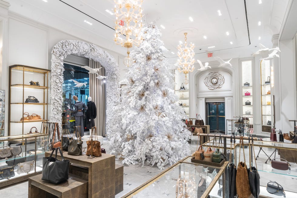 a flock of white plaster geese flies across the room of a luxury store, with a large, white christmas tree in the background.