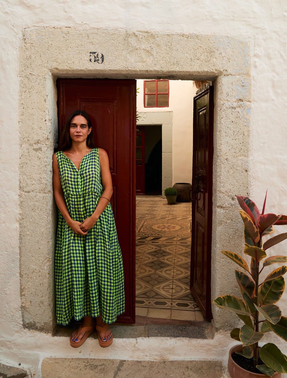 A person standing at the entrance of a building wearing a green checkered dress.