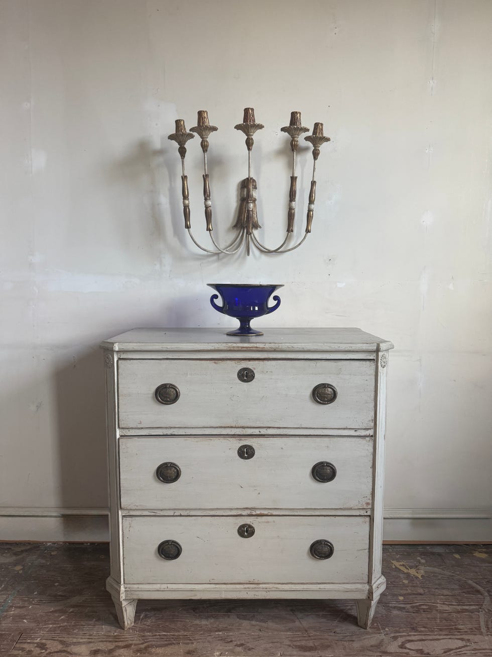 A vintage white dresser with a blue decorative bowl and a wall-mounted candelabra.