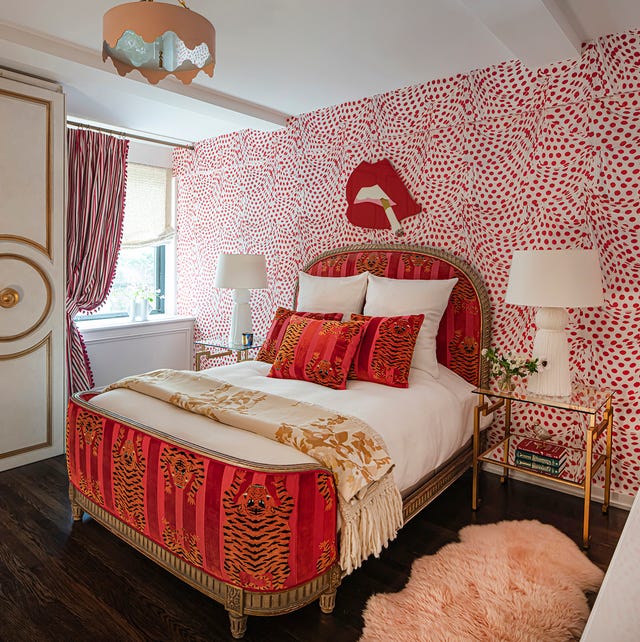 A-List 2024 - ELLE DECOR bedroom with a empire styled bed with red striped velvet footboard with tiger print and matching oval headboard and pills with white sheets and a glass side table and white lamp and dark wooden floor