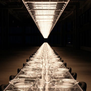 A long, elegantly set dining table illuminated by overhead lights.