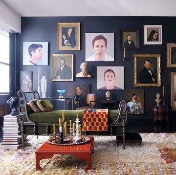 a stylish room featuring a variety of paintings on the wall a green chaise lounge wooden furniture and decorative elements