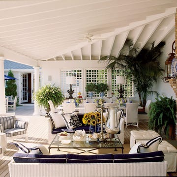 a large outdoor room with a large patio and a large patio with white chairs and brick fireplace and plant in the background