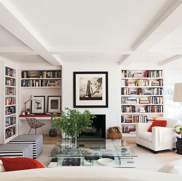open living room painted in white with open shelves and fireplace and ottomans and glass table in the center and black and white prints