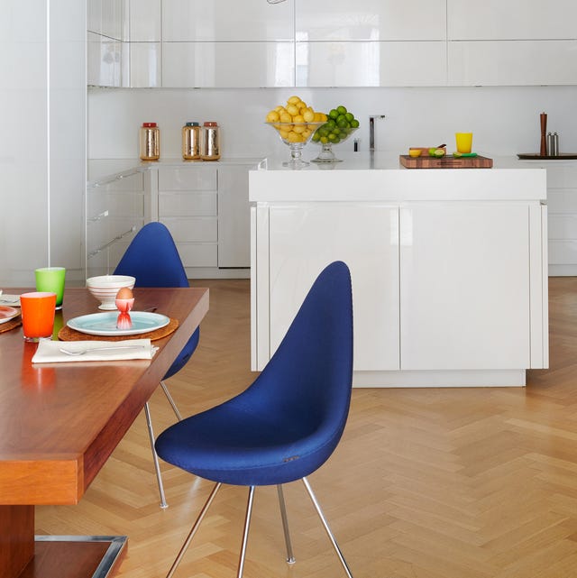 A-List 2024 - ELLE DECOR a kitchen with a honey colored table and blue chairs and a white lacquer counter with sink and cabinets at back and a light chevron pattern floor