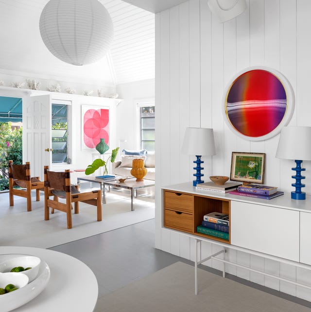 A-List 2024 - ELLE DECOR white living area with white console and blue lamps and wood chairs and a glass cocktail table