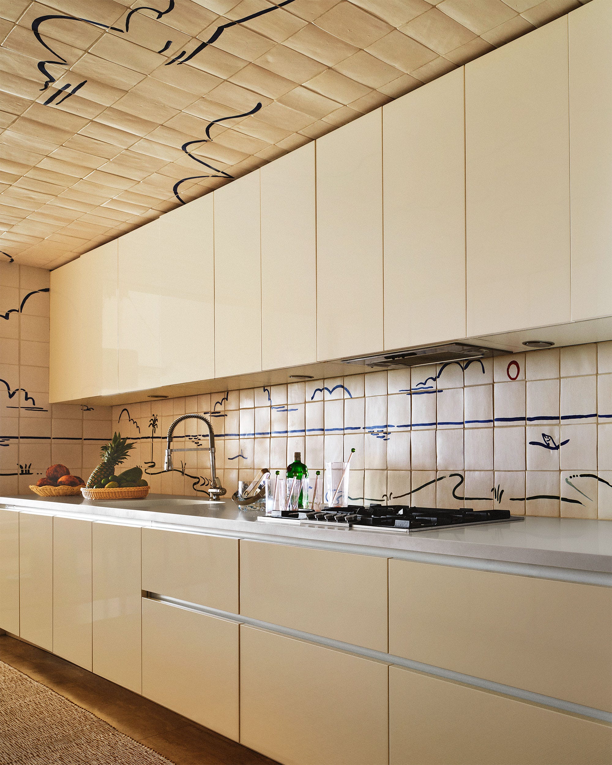 a kitchen with glossy ivory colored cabinets above and below a light counter with a stovetop and sink backsplash wall and c