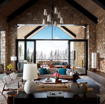 great room with high ceilings and large glass windows and a fireplace on the right and a furniture and seating gathering in the center and a view of the snowy mountains