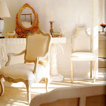a room with a gilt mirror on a white console and carved chairs