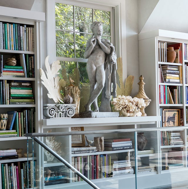 A-List 2024 - ELLE DECOR glass wall staircase with a landing made of built in bookcases full of books and a classical statue at center