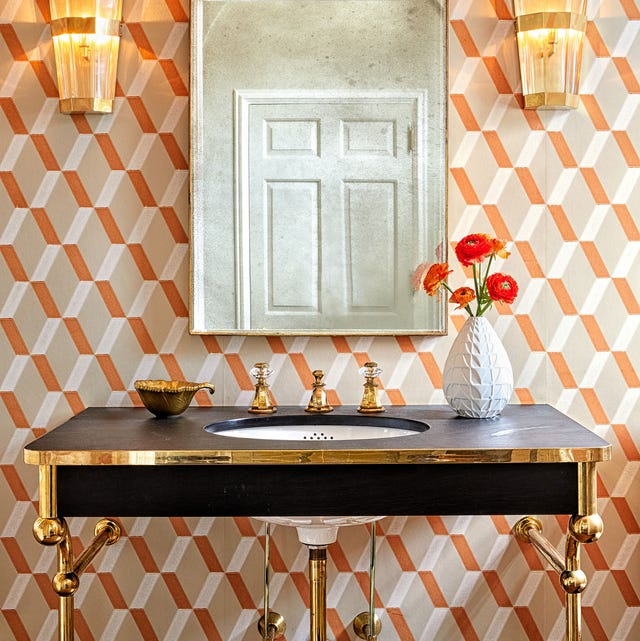 A-List 2024 - ELLE DECOR black sink with metal legs and hardware against a patterned orange and white wallpaper and art deco looking sconces on either side of a long mirror