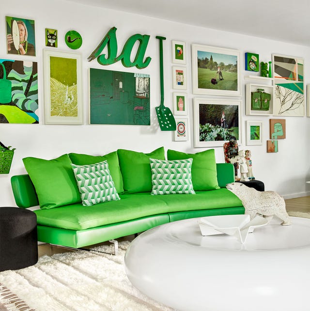 A-List 2024 - ELLE DECOR a living room with a curvey neon green sofa and a large round donut shaped white cocktail table and artwork on the wall in white frames and green accented artwork and a dark black round side table