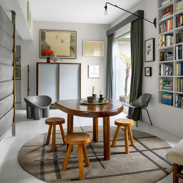 A-List 2024 - ELLE DECOR clean white dining area with natural style three legged dining table and low wood three legged stools and a round geometric r