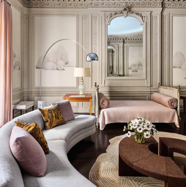 A-List 2024 - ELLE DECOR parisian living area with richly molded walls and ceilings and a curvaceous sofa and a daybed at back and a sectional low round coffee table at center