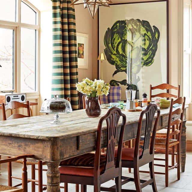 a rustic dining room table with chairs and a green and cream striped curtains at the window and a large painting of an artichoke in a vivid green at the back and a star chandelier overhead a rustic dining room table with chairs and a green and cream striped curtains at the window and a large painting of an artichoke in a vivid green at the back and a star chandelier overhead