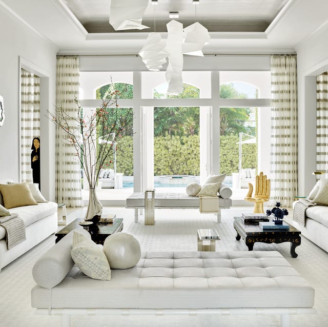 A-List 2024 - ELLE DECOR a all white living room with matching white sofas facing each other and a chaise longue in the foreground with a large window opening to a pool in the back and mat