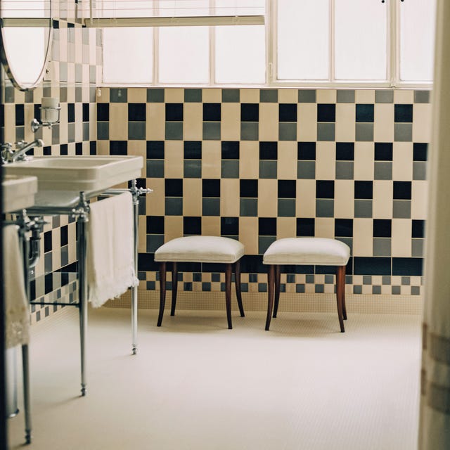 A-List 2024 - ELLE DECOR a bathroom with black and gray and cream grid tiles with a vanity on silver legs and stools