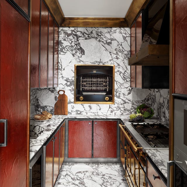 A-List 2024 - ELLE DECOR long galley kitchen with grey and white marble floor and counter and walls and red cabinets with some gold hardware