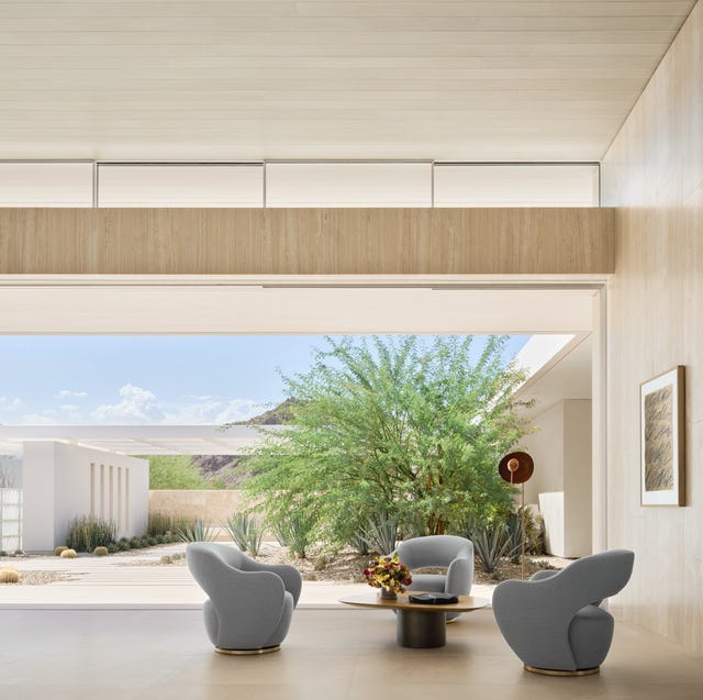 A-List 2024 - ELLE DECOR large open living area with three gray chairs around a low pedestal cocktail table and a large bushy tree in the opening