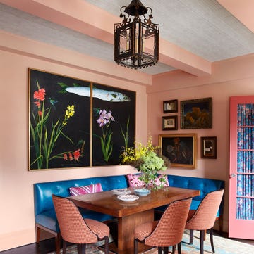 a light pink dining room with built in blue leather banquette, wood table, and three chairs in a spice colored fabric, large diptych of flowers and fish, small framed art, antique metal pendant, oriental rug