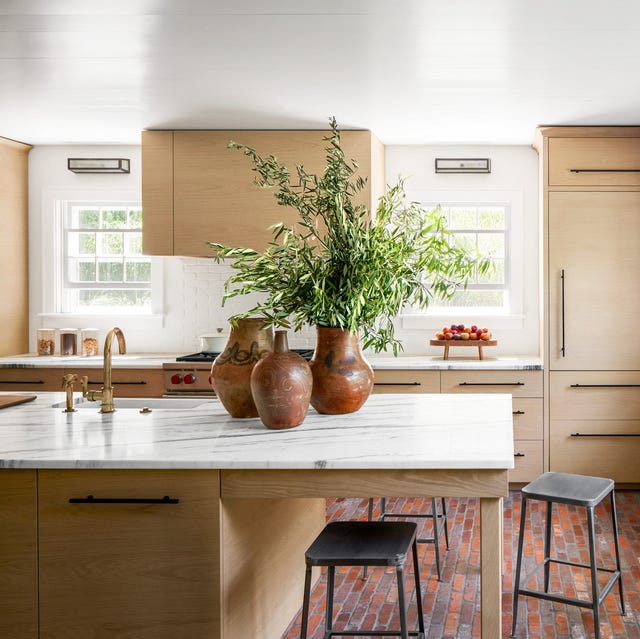 A-List 2024 - ELLE DECOR a light wood kitchen with a plant in one of three terra cotta vases on the counter and some metal stools