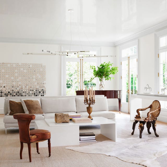 A-List 2024 - ELLE DECOR a very white airy living room with a white sofa and a table and unusual dark stained armchairs