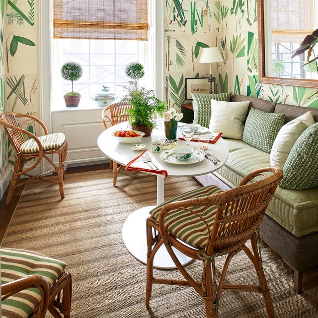 A-List 2024 - ELLE DECIR a cozy seating area with white pedestal table set with breakfast plates and cups and a leafy wallpaper and rattan chairs with striped pillow seats and a sofa with platform and velvety light green cushion