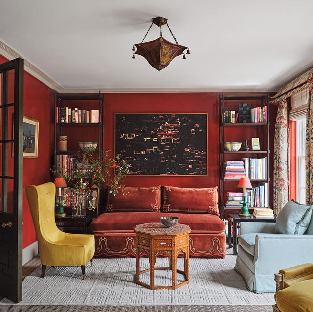 A-List 2024 - ELLE DECOR a red painting living room with a red sofa flanked by etageres and small yellow chair and a light blue love seat and a small octagon table as a cocktail table