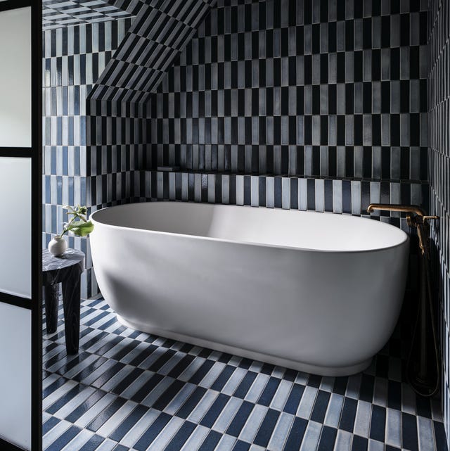 A-List 2024 - ELLE DECOR black and grey skinny tile bathroomwith a white standalone tub against the back wall