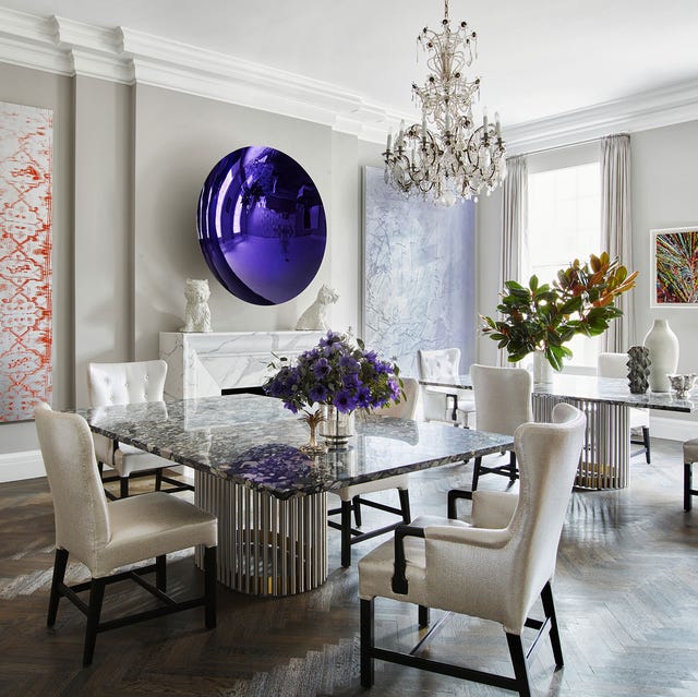 A-List 2024 - ELLE DECOR a very white dining room with a chandelier and a table with chairs and a large oval purple artwork over the fireplace mantel