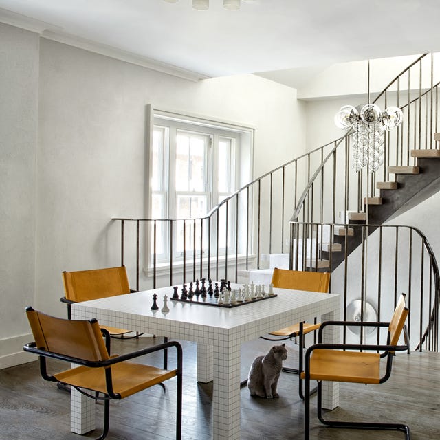 A-List 2024 - ELLE DECOR a white blocky game table with yellow chairs on an open landing with swoopy staircases going up and down
