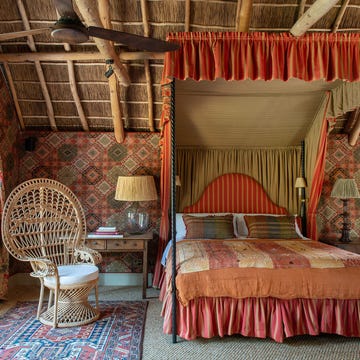 a canopy bedroom with a bed and a wicker chair and patterened walls in an orange and red tone
