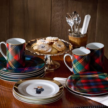 sets of ralph lauren dinnerware, including gold rimmed plates with the polo bear and plaid printed plates on a dark wood table.