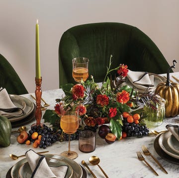 lush and abundant thanksgiving centerpiece with florals, candles, a pumpkin, and velvet upholstered dinner table chairs