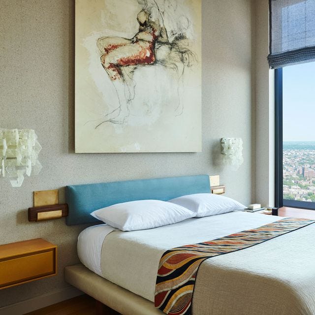 A-List 2024 - ELLE DECOR a bed with a blanket on it and artwork over the bed and a skinny horizontal blue velvet headboard mounted over a wood frame