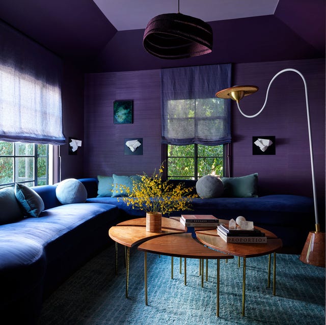 A-List a living room with dark purple walls and a dark blue wraparound sofa and round sectional coffee table and a swooshy standing lamp