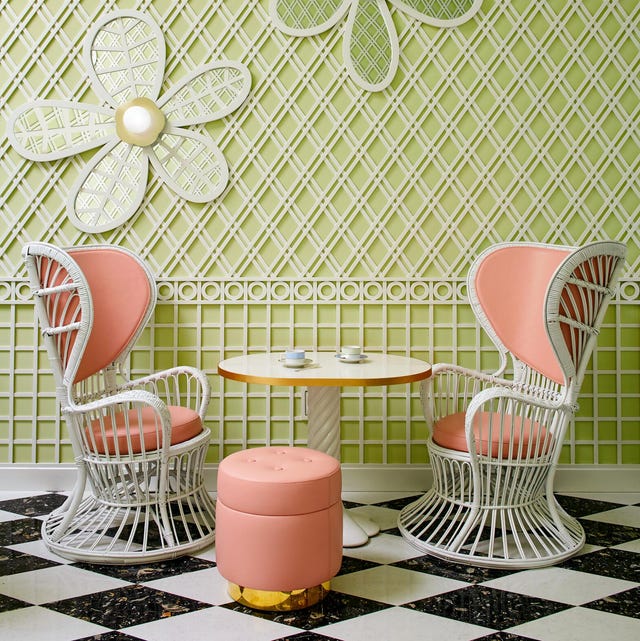 A-List 2024 - ELLE DECOR garden room with light green walls with lattice overlaid on it with daisy designs and a small white pedestal table flanked by two modern white garden wicker chairs with peachy colored cushion backs and seats and a small round stool in the same fabric with a gold base