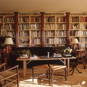 large living room with wall to wall pine bookshelves punctuated by carved wooden columns and assorted sofas and wood chairs and a sisal like carpet in a neutral color