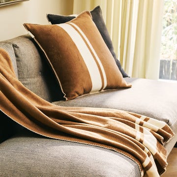 a camel throw blanket and pillow on a gray couch. a camel throw blanket and pillow on a gray couch.