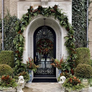 a fancy front porch marked by greenery, trimmed hedges, a metal gate door, and more